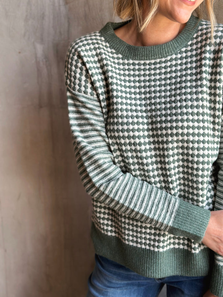 Person wearing a green and white patterned sweater against a neutral background