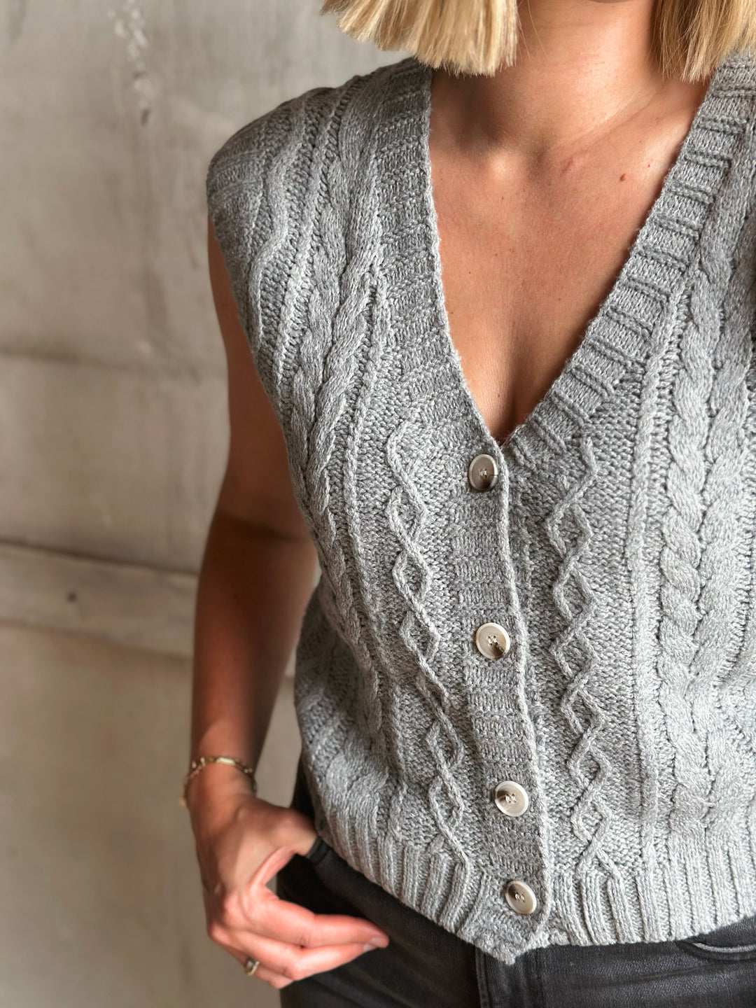 Person wearing a gray knitted vest with a textured pattern against a neutral background