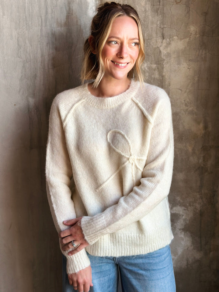Woman wearing a cream sweater with a heart design against a textured wall.