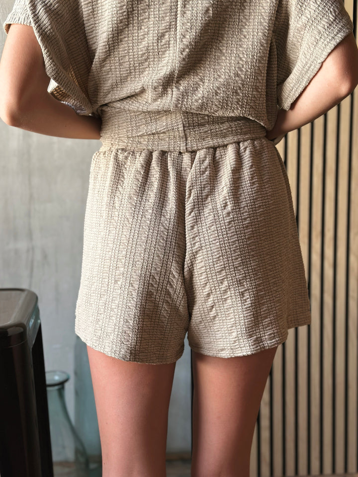 Back view of model wearing textured knit top & shorts set with elastic waist in the color taupe