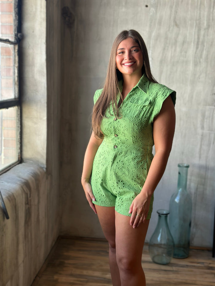 Woman wearing a green outfit standing in a room with large windows and a concrete wall.