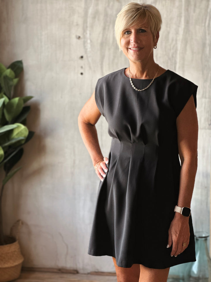 Woman wearing a black dress standing indoors with a neutral background