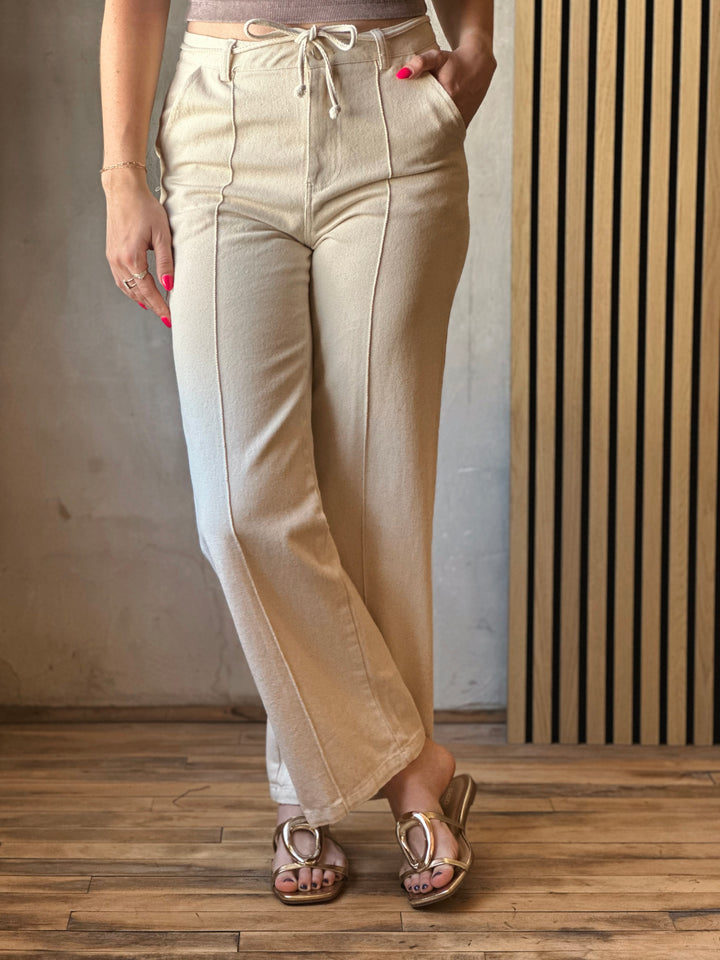Front view of model wearing Tie Waist Pants in a oatmeal hue with front pintuck seams and tie waist