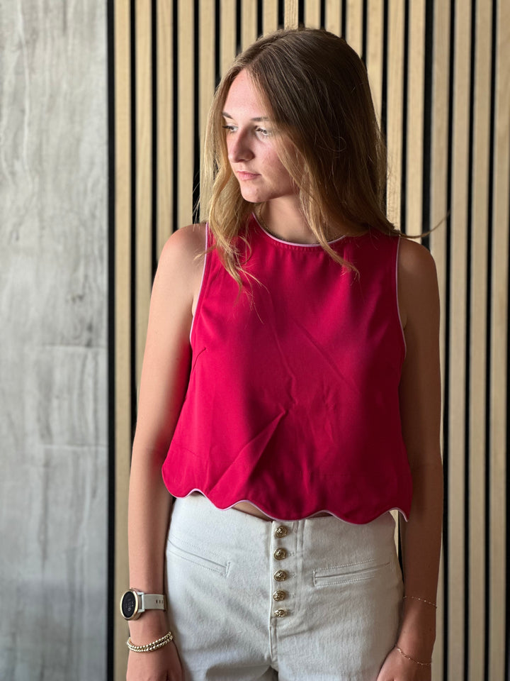 Front view of model wearing a scarlet colored top with a sleeveless design and scalloped hem and a button closure on the back of top