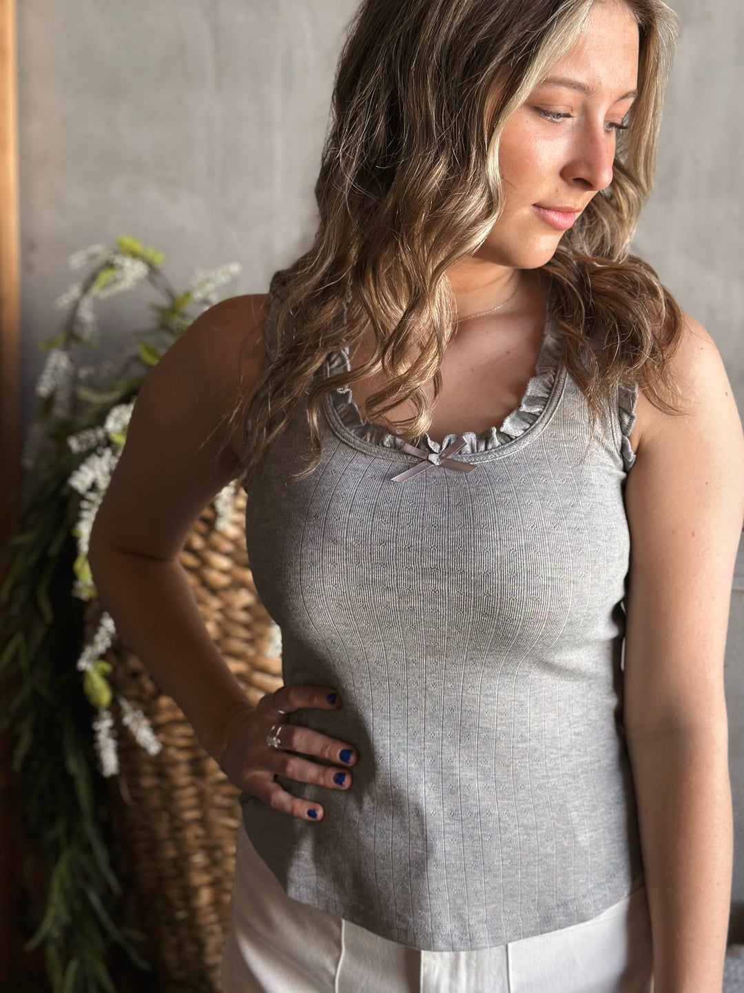 Front view of model wearing a bow trimmed ruffle tank top with a round neckline and a sleeveless design in the color heather