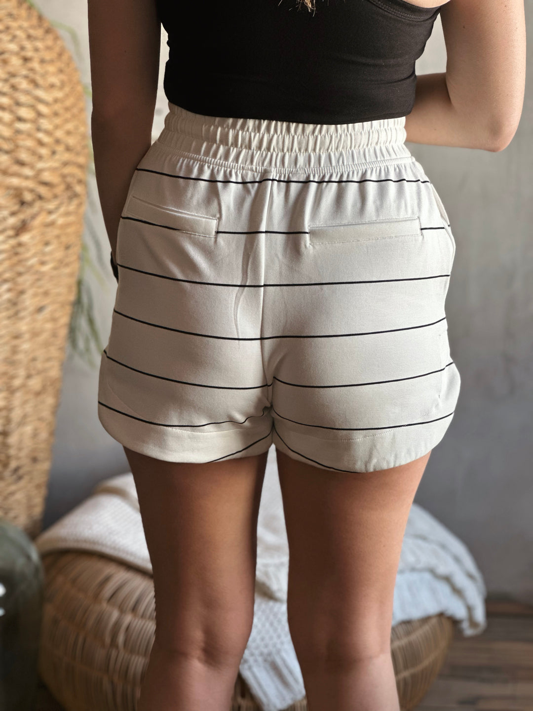 Back view of model wearing shorts with a drawstring elastic waistband, that also has side and back pockets they are the color cream with black stripes
