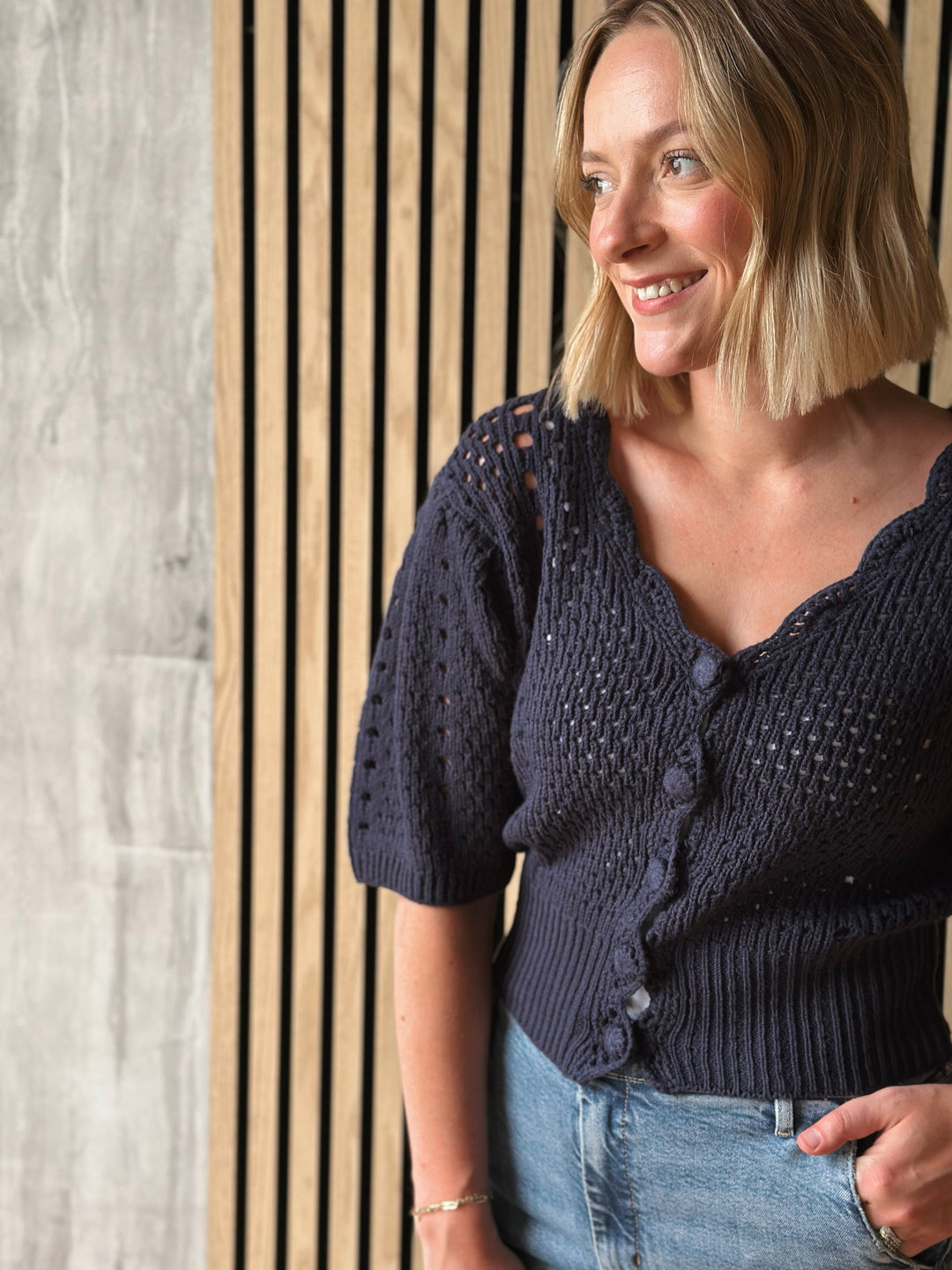 Woman wearing a dark blue knitted cardigan standing against a wooden panel background