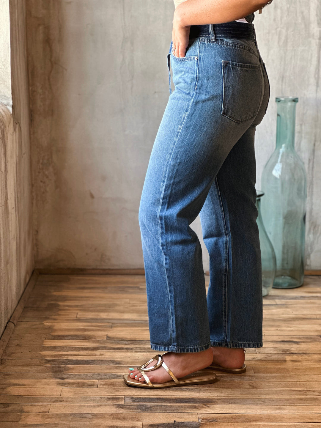 Person wearing blue jeans standing on a wooden floor with a neutral wall background