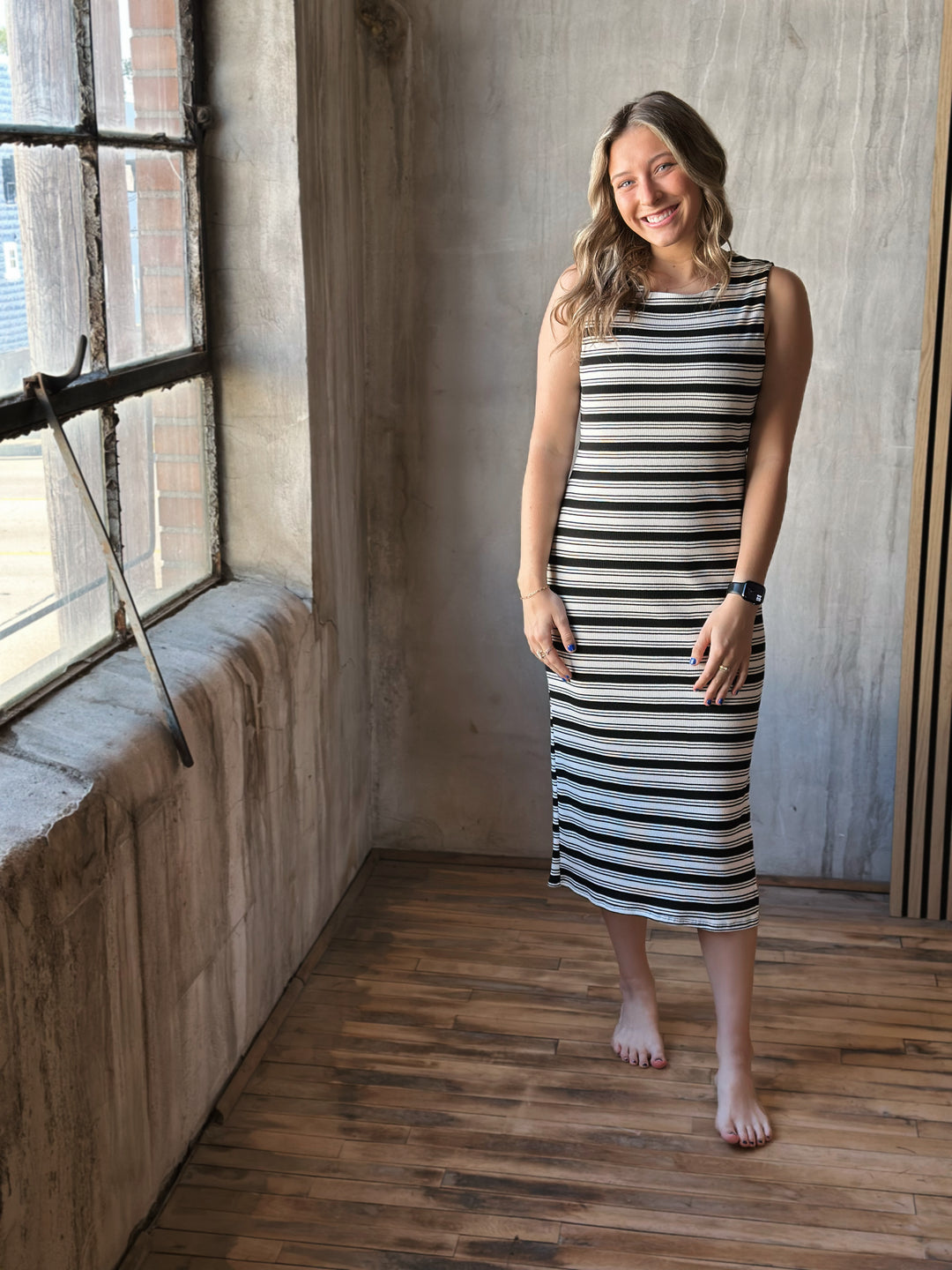 Front view of model wearing a sleeveless ribbed midi dress with black and white stripes, a rounded neckline, and a cut out back detail