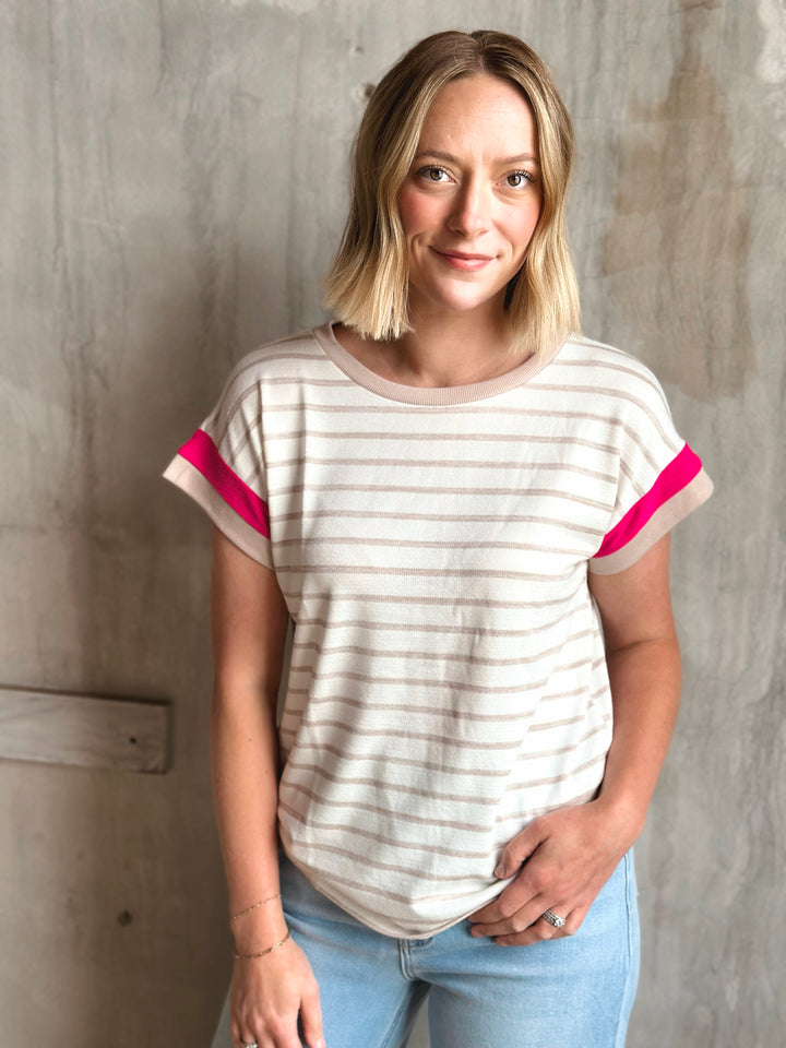 Woman wearing a striped t-shirt with pink accents against a textured wall.