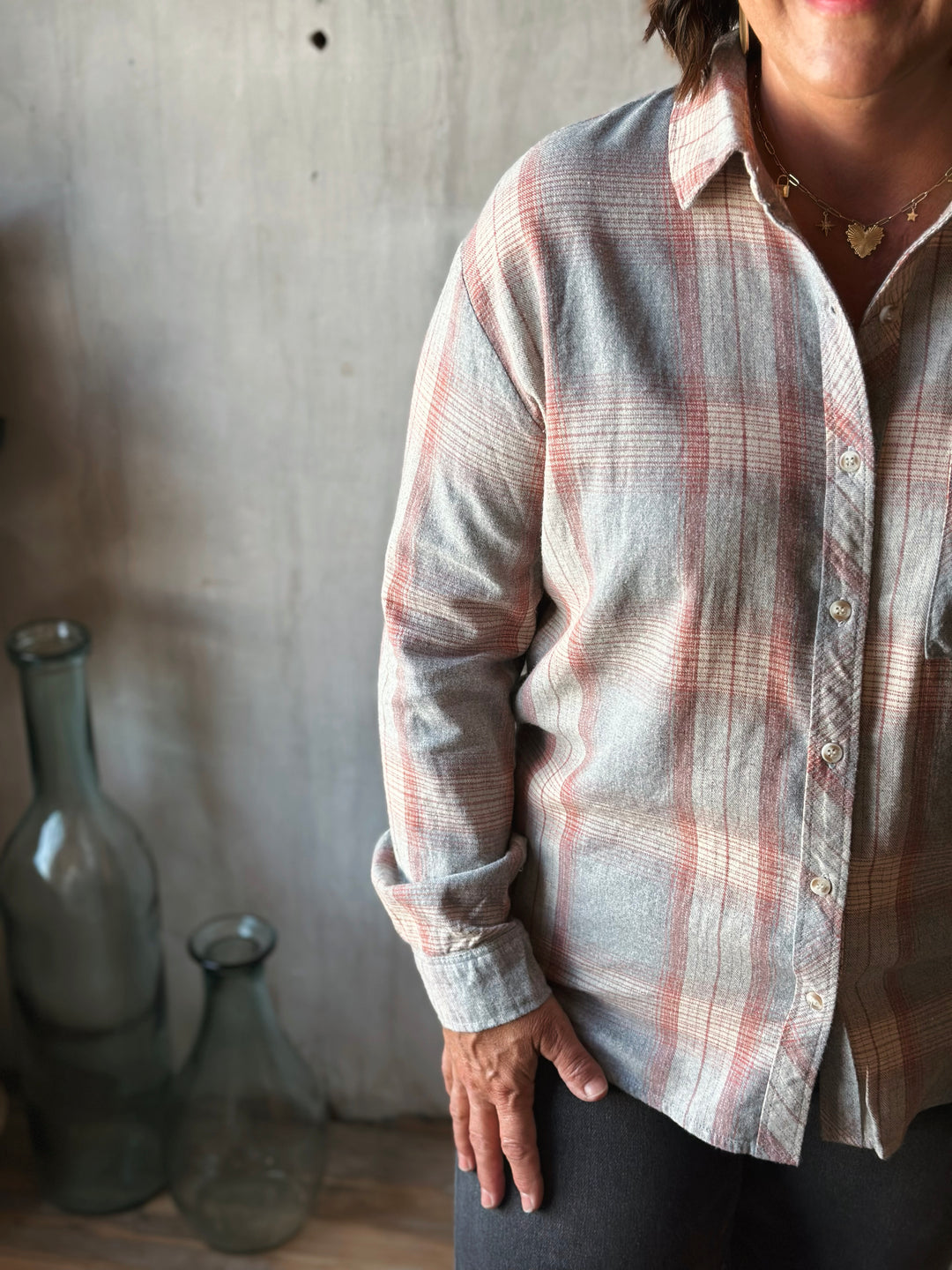 Person wearing a plaid shirt with a neutral background and two glass bottles.