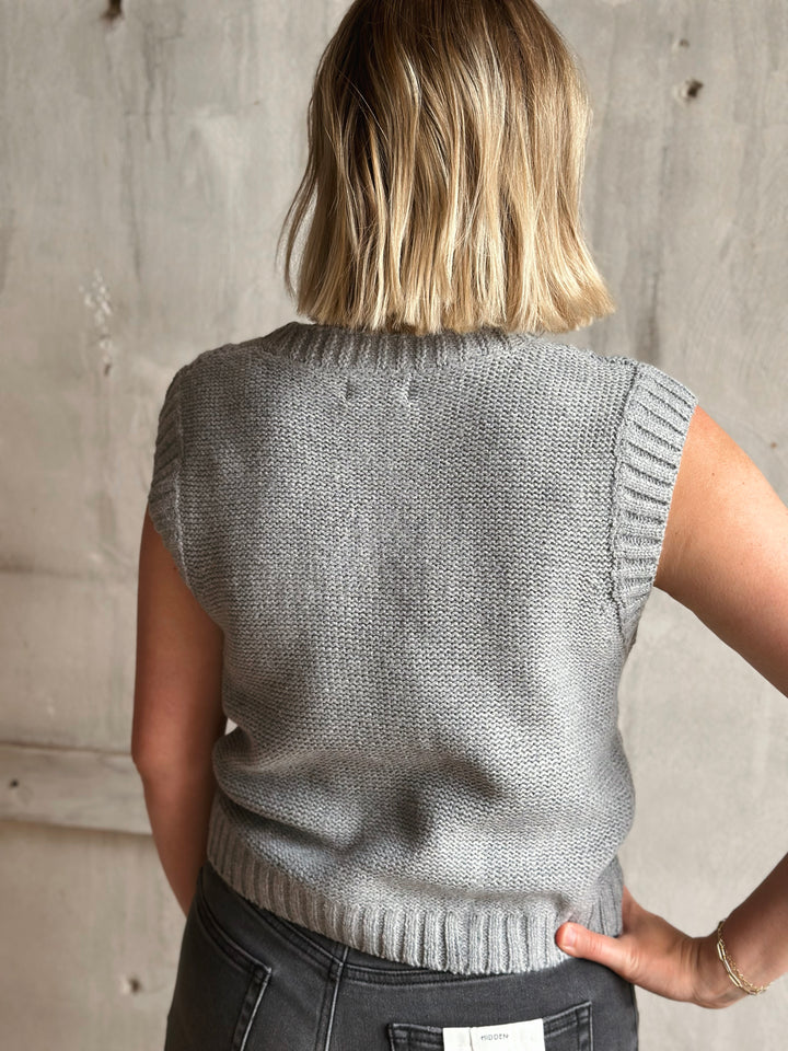 Person wearing a gray knitted vest against a concrete wall.