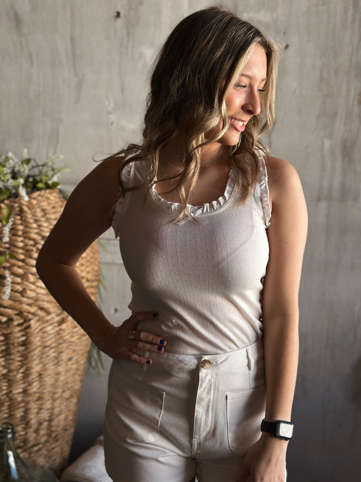 Front view of model wearing a bow trimmed ruffle tank top with a round neckline and a sleeveless design in the color white