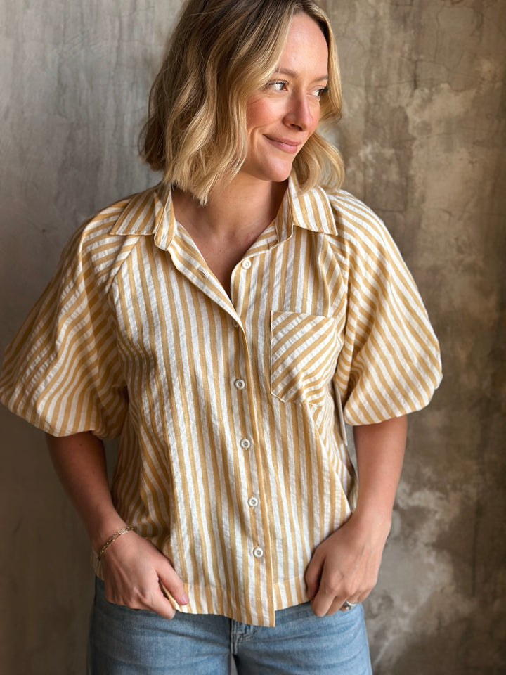 Woman wearing a yellow and white striped shirt against a textured wall.