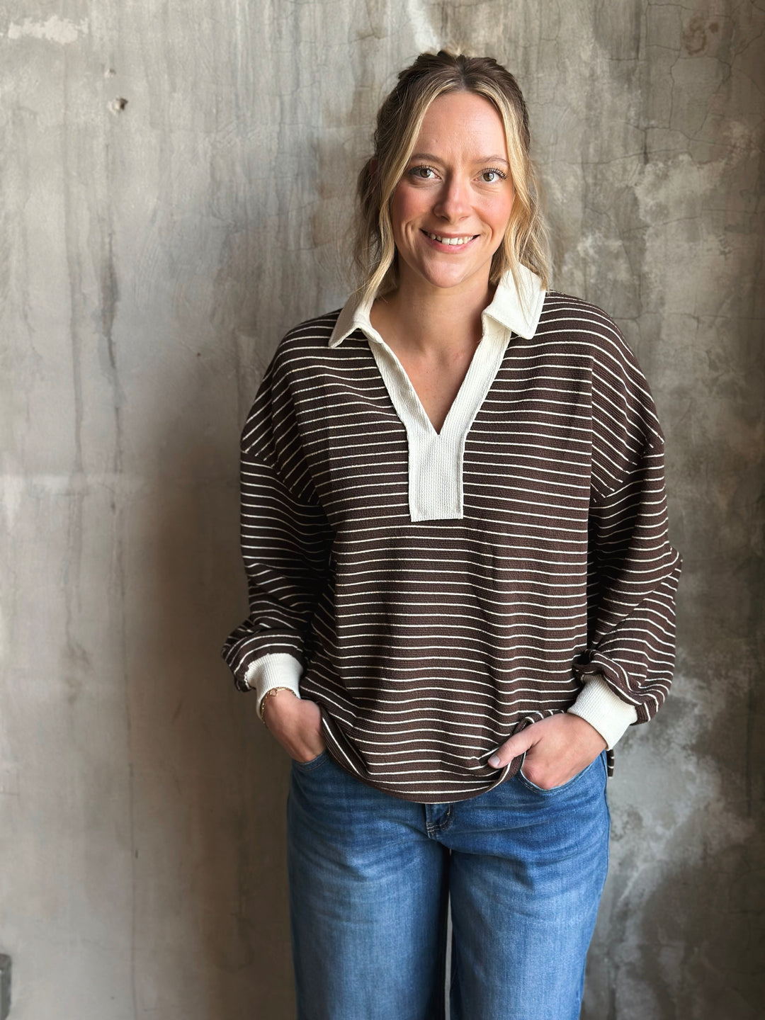 Woman wearing a striped shirt and jeans against a textured wall