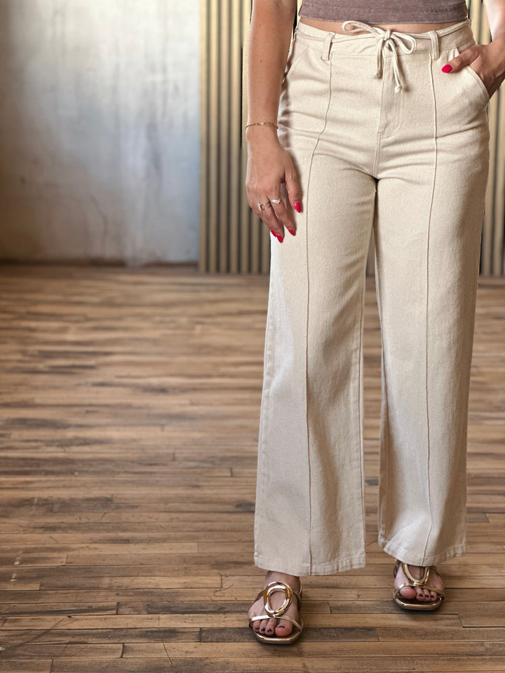 Front view of model wearing Tie Waist Pants in a oatmeal hue with front pintuck seams and tie waist