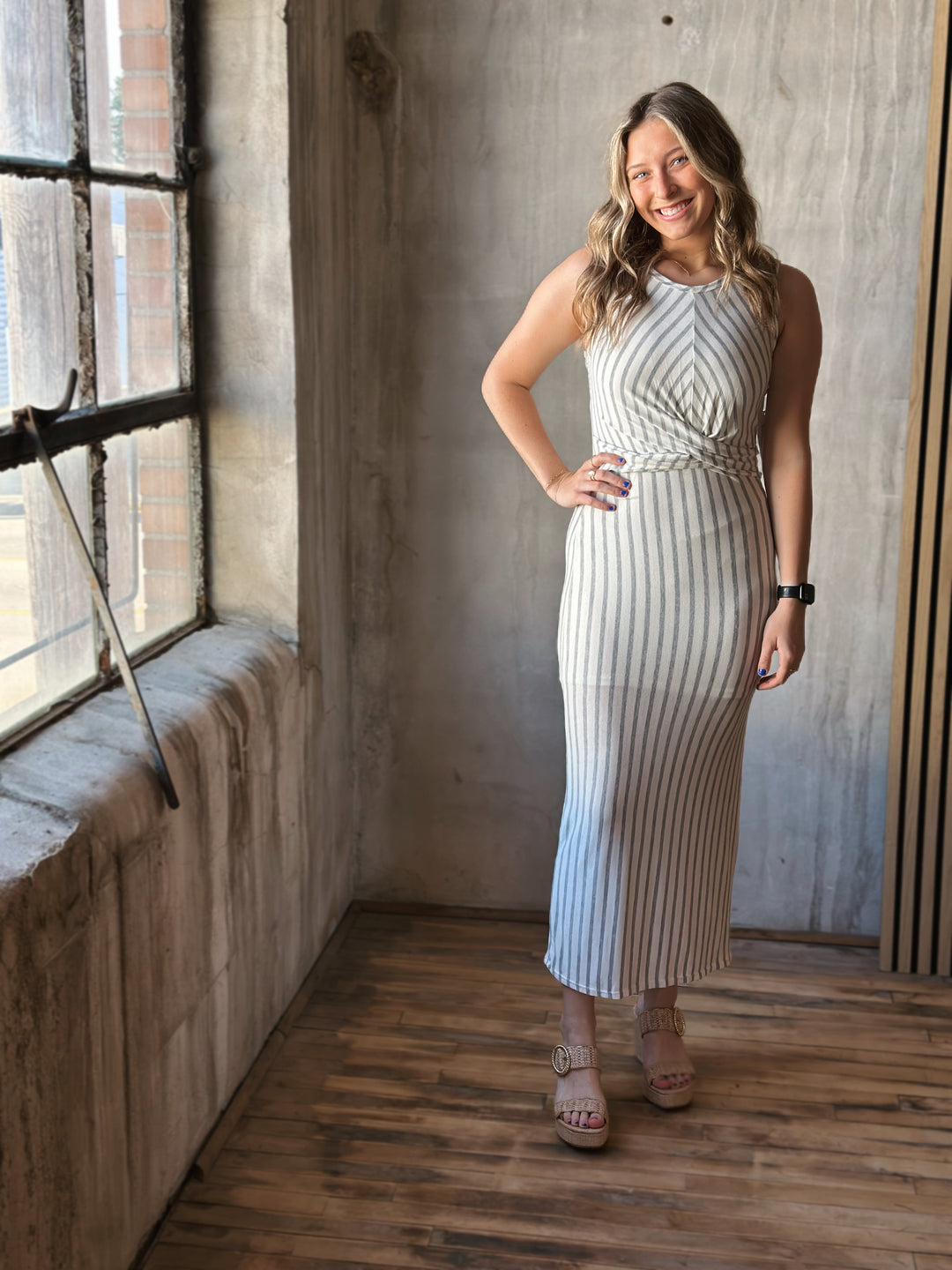 Front view of model wearing a front twist sleeveless dress with white and heather gray stripes and a rounded neckline