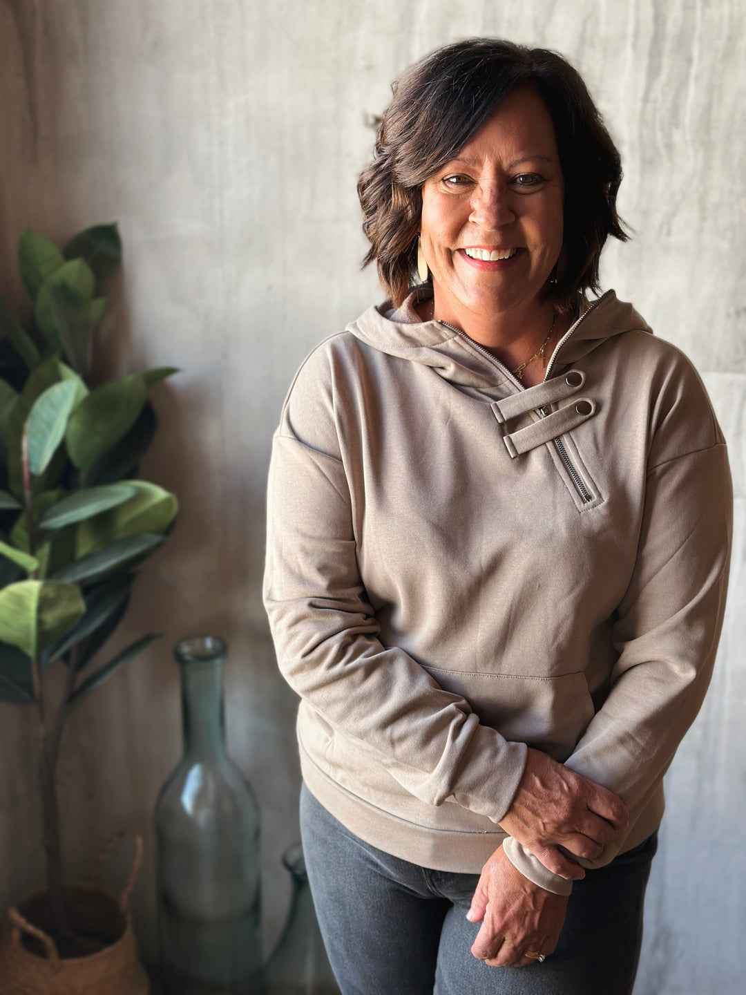Woman wearing a beige hoodie standing indoors with a neutral background