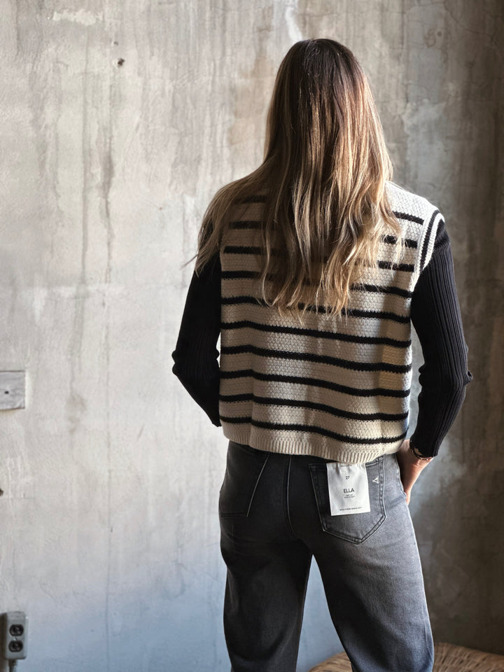 Person wearing a striped vest with a visible brand tag against a concrete wall.