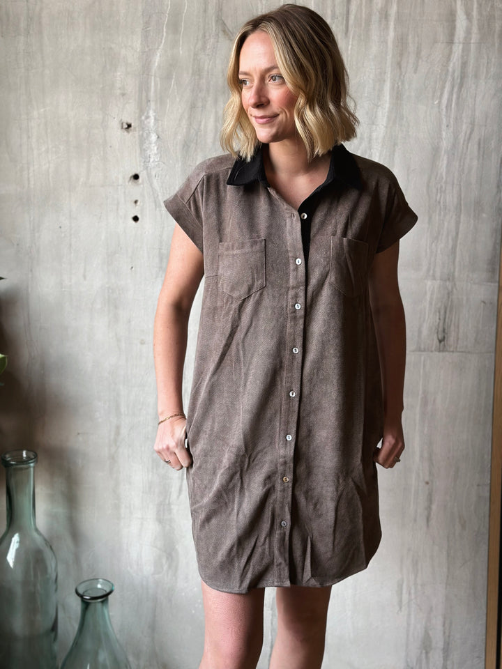 Woman wearing a brown button-up dress against a concrete wall.