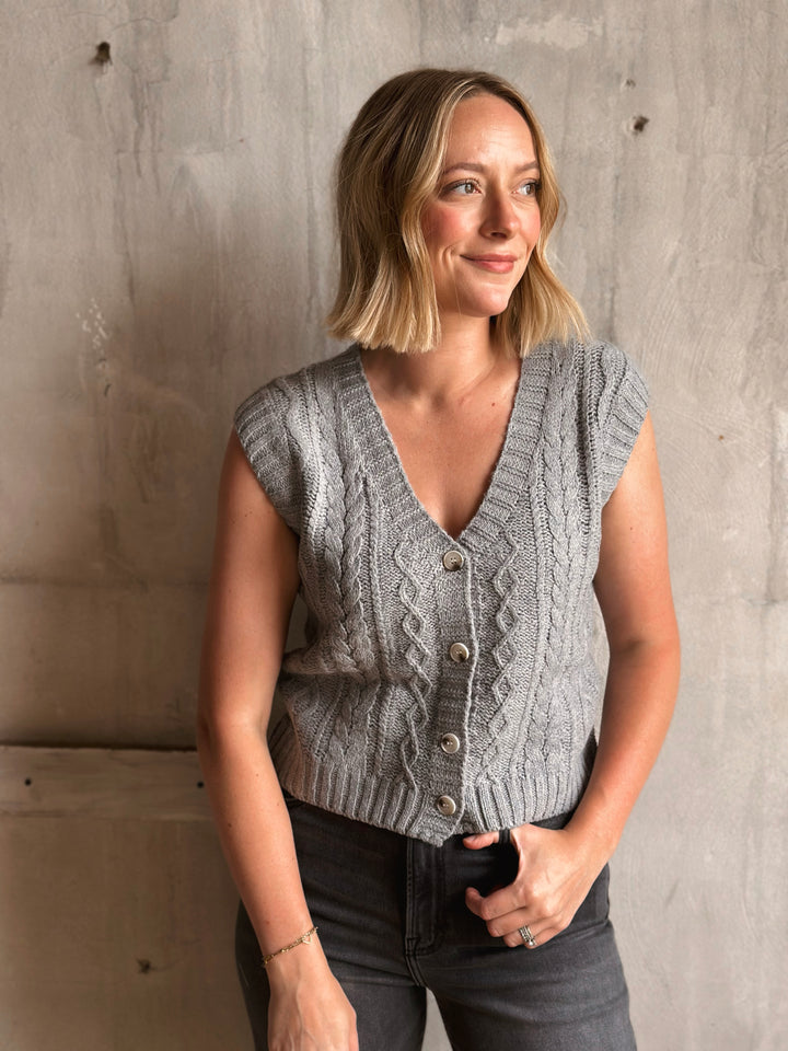 Woman wearing a gray knitted vest against a concrete wall