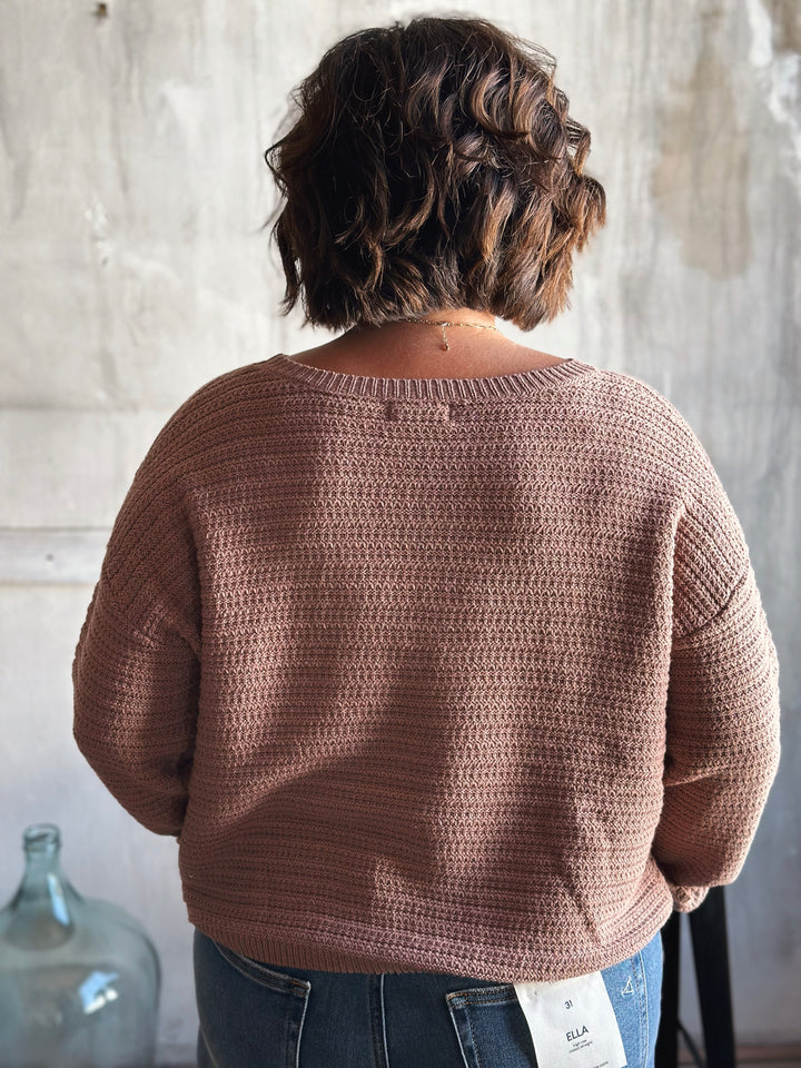 Person wearing a brown crochet sweater against a neutral background