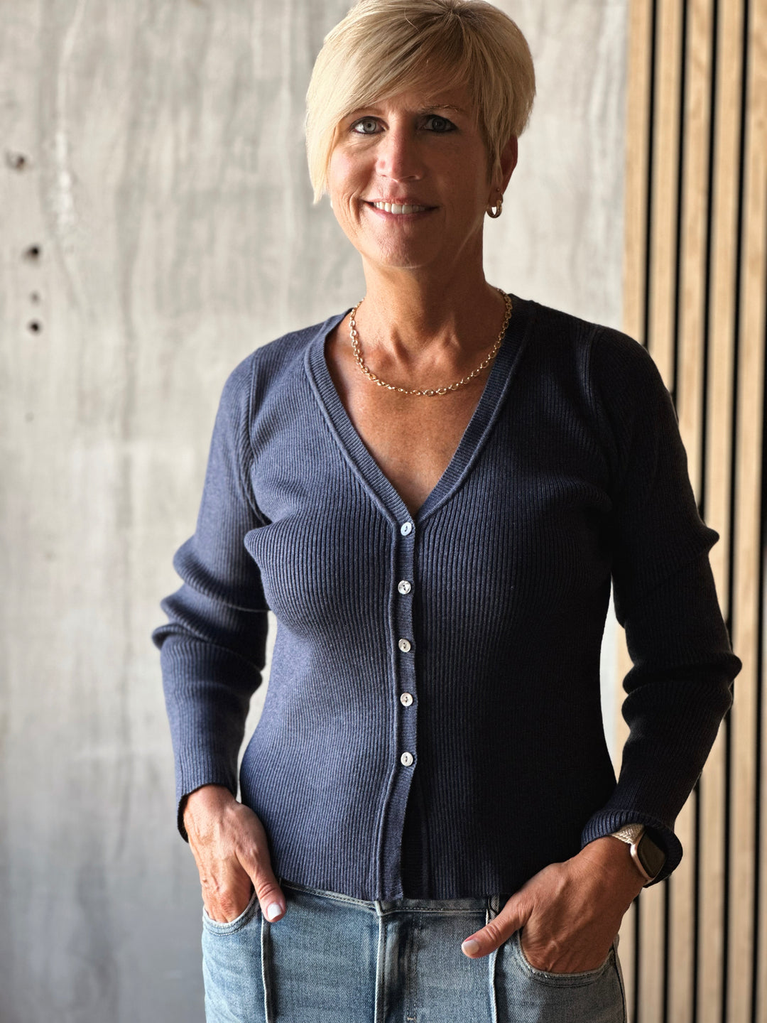 Woman wearing a blue cardigan and jeans standing against a neutral background