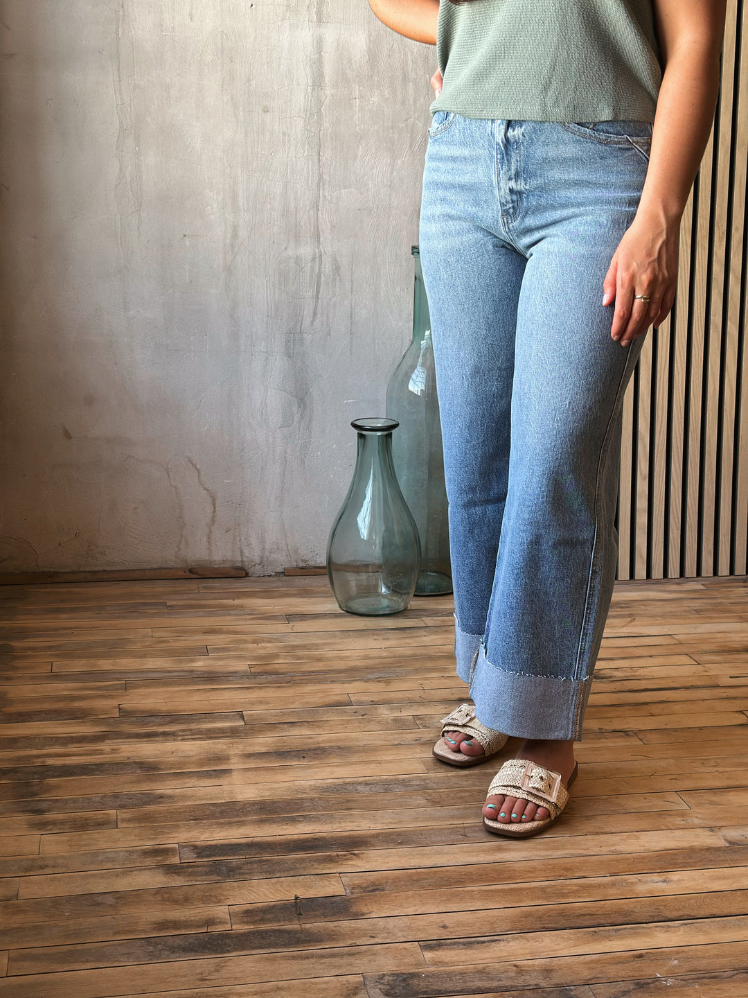 Person wearing light blue jeans standing on a wooden floor with a vase in the background.