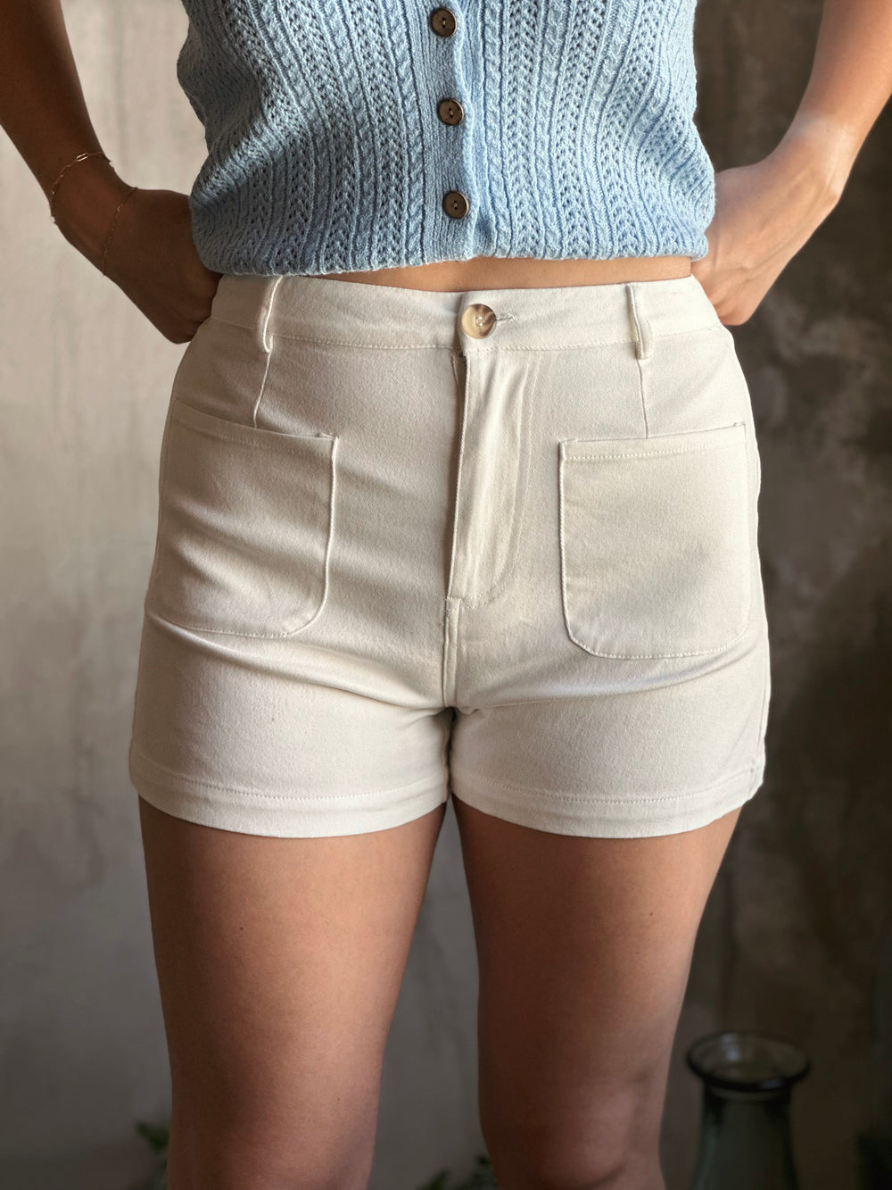 Front view of high waist white shorts, designed with classic button-zipper closure and front patch pockets