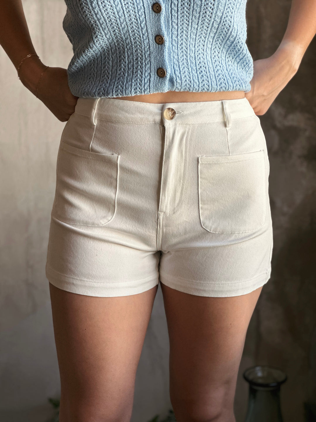 Front view of high waist white shorts, designed with classic button-zipper closure and front patch pockets