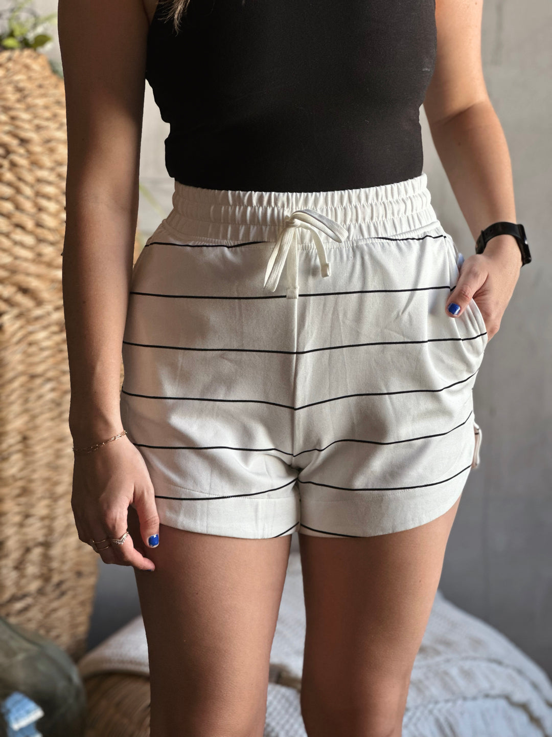 Front view of model wearing shorts with a drawstring elastic waistband, that also has side and back pockets they are the color cream with black stripes