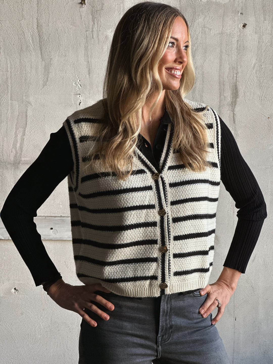 Woman wearing a striped cardigan over a black shirt against a concrete wall.