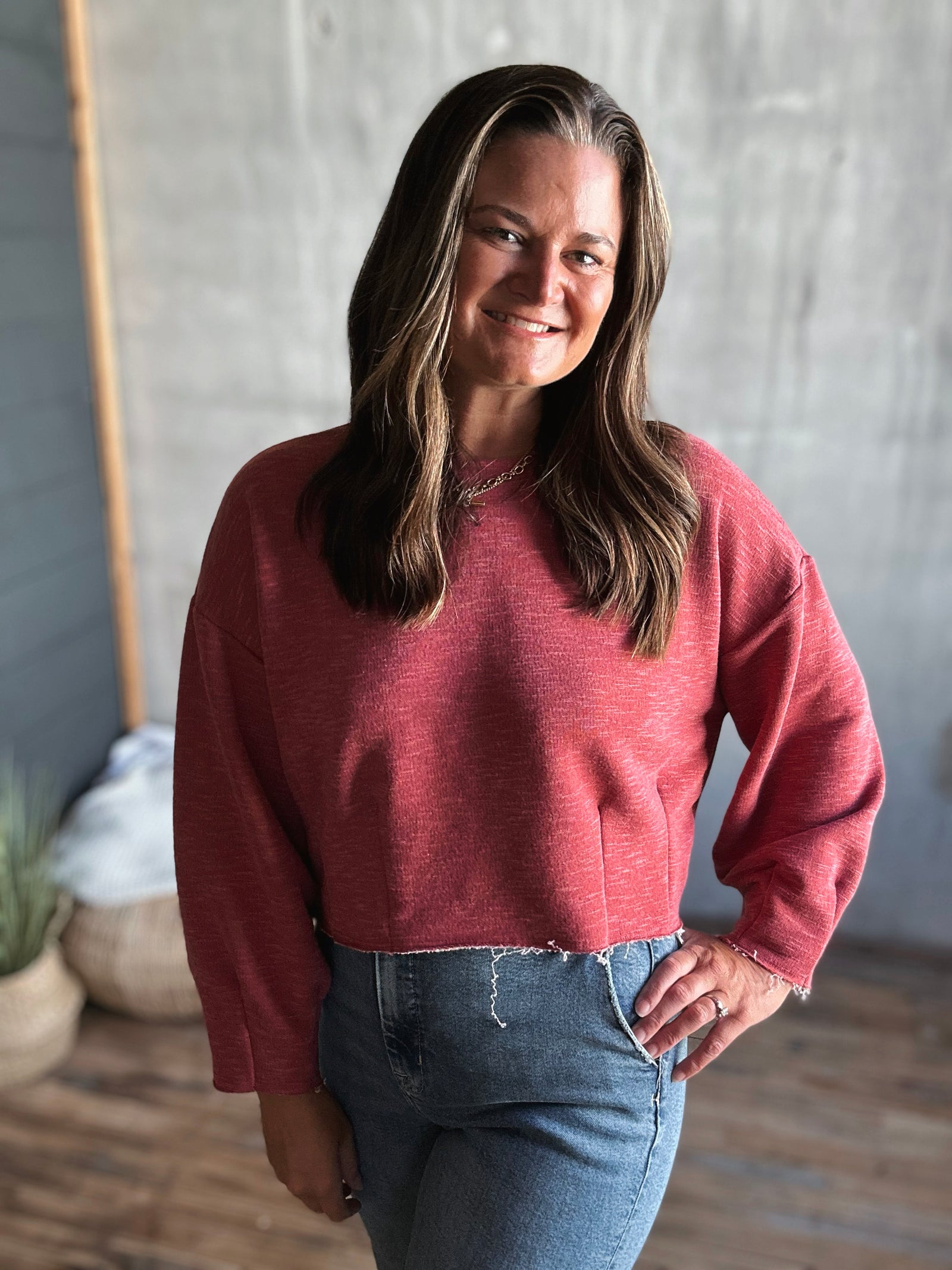 Woman wearing a pink sweater and blue jeans standing against a neutral background