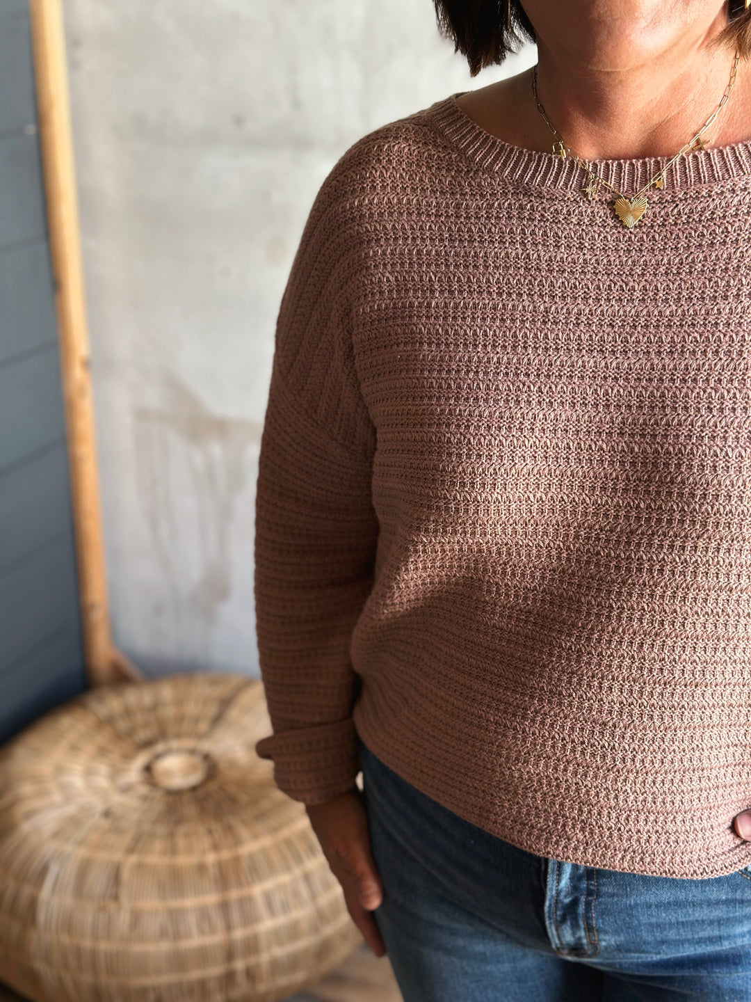 Person wearing a brown knitted sweater with a blurred background