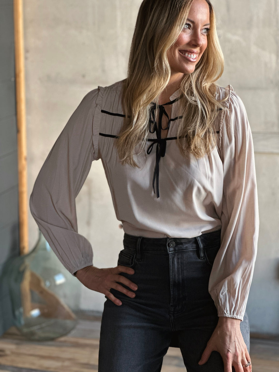 Woman wearing a beige blouse with black lace details and black pants in an indoor setting.