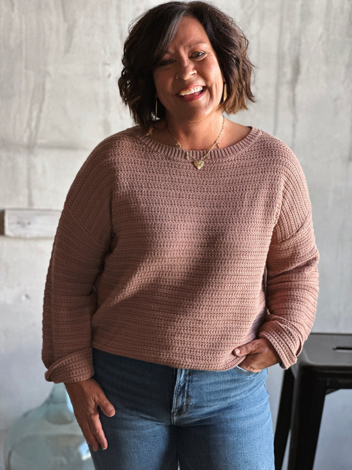 Woman wearing a brown crochet sweater against a neutral background