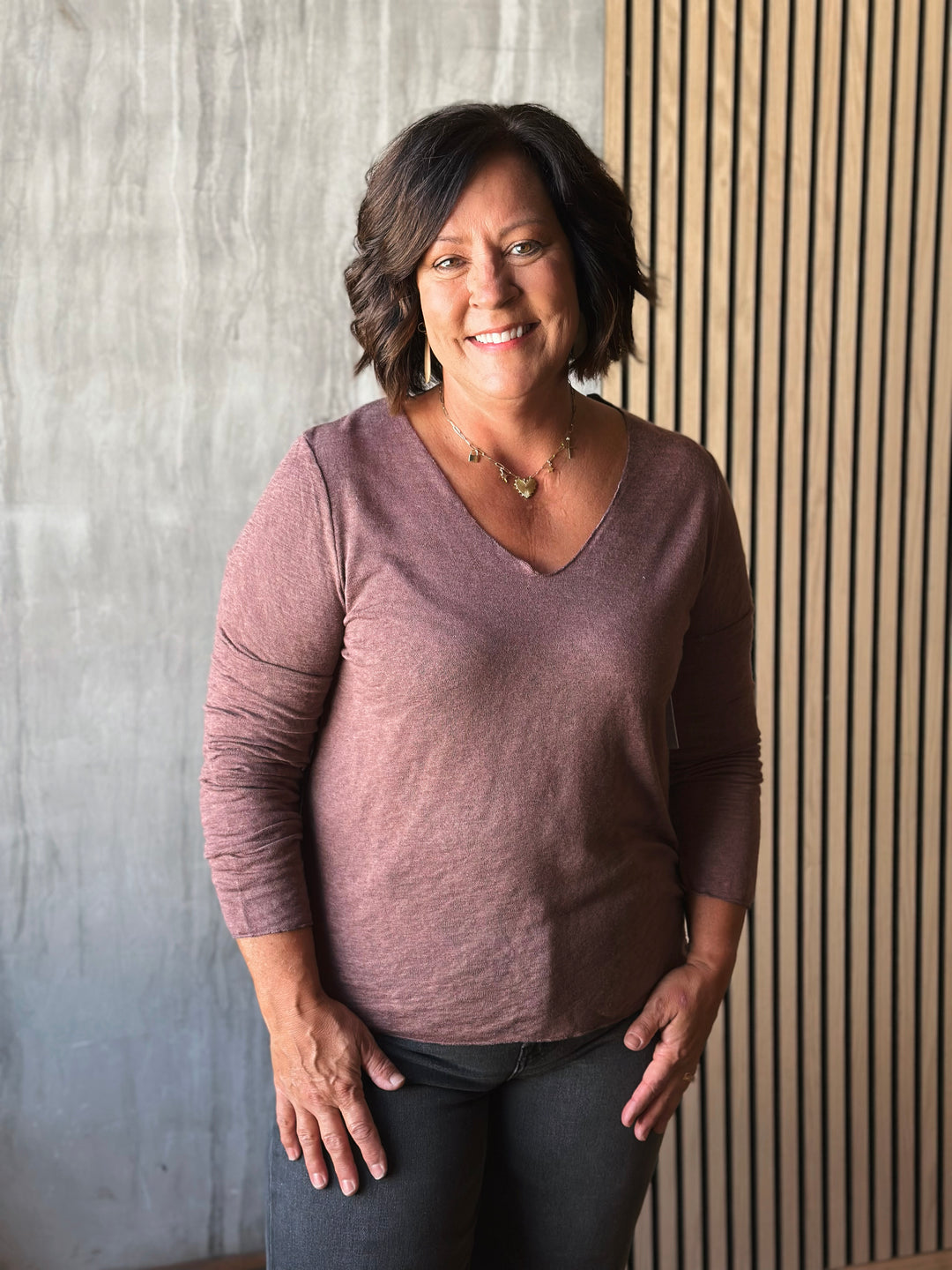 Woman wearing a purple shirt standing against a textured wall.