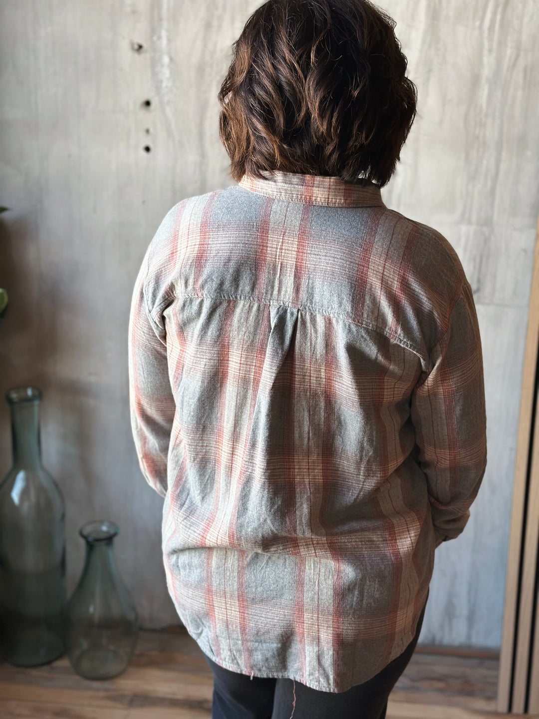 Person wearing a plaid shirt in a room with a textured wall and glass bottles.
