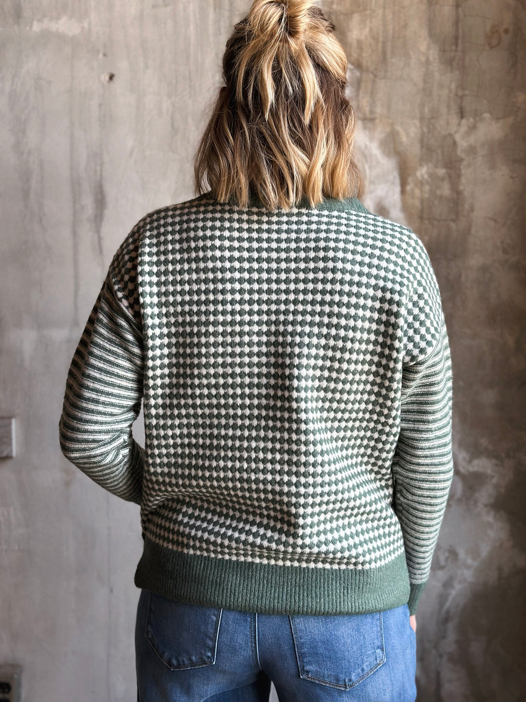 Person wearing a houndstooth patterned sweater with a concrete wall background