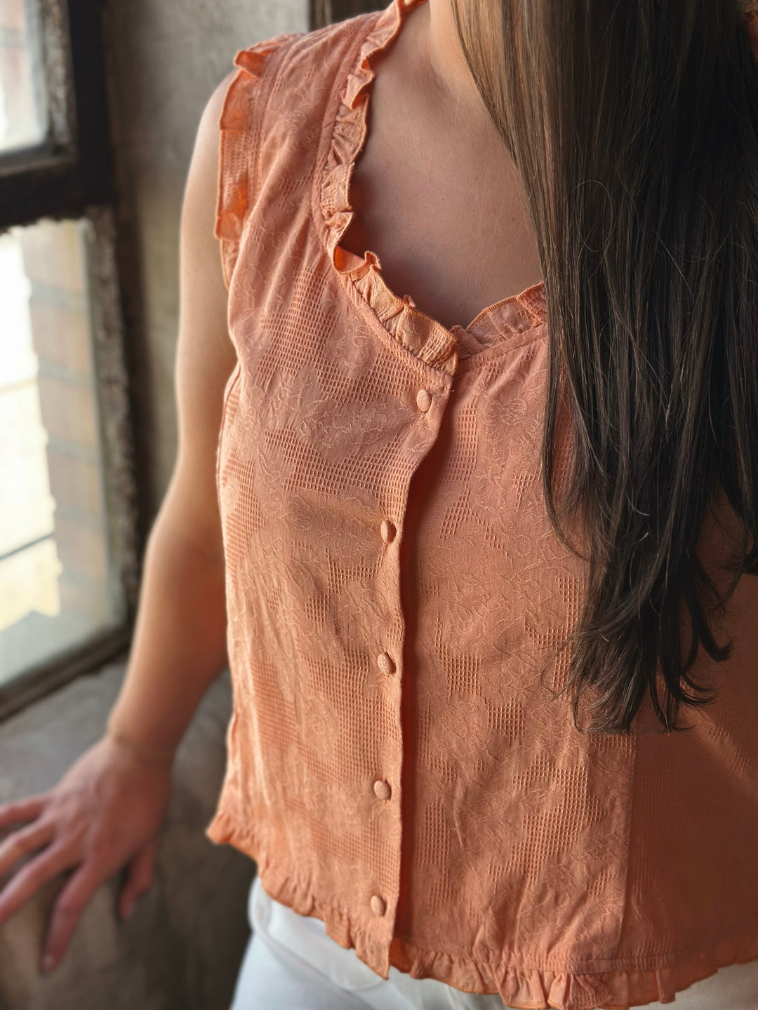Person wearing a peach-colored blouse with ruffled details, standing indoors.