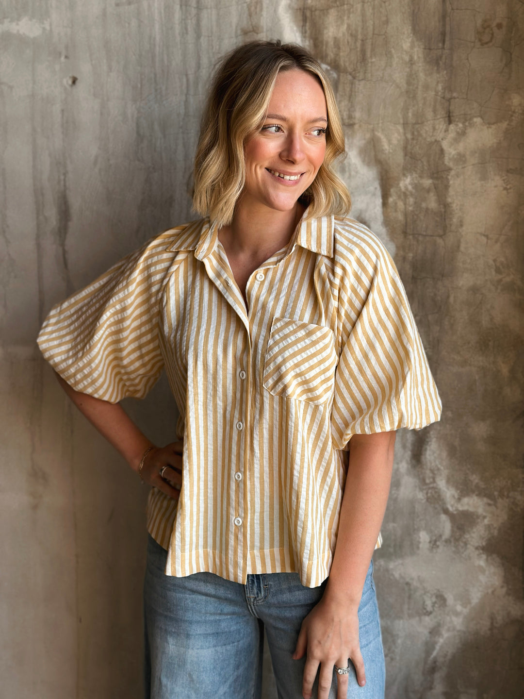 Woman wearing a striped shirt and jeans against a textured wall.