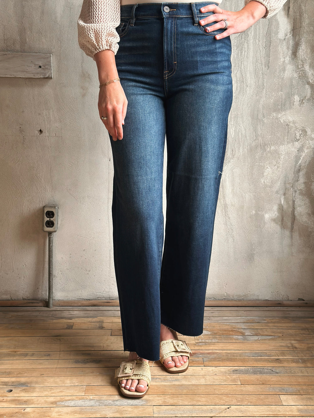 Person wearing blue jeans standing against a textured wall.