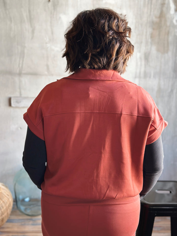 Person wearing a rust-colored jacket standing in a room with a neutral background