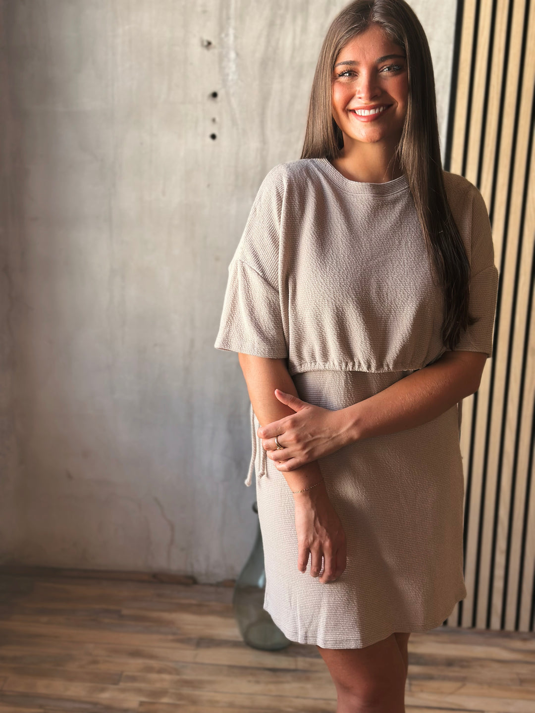 Woman wearing a beige dress standing against a textured wall.