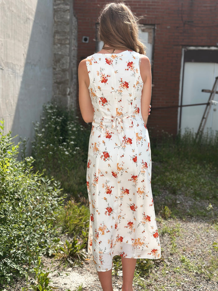 Back  view of model wearing midi dress with floral print in ivory with multicolored flowers, it also has a button down front and a sleeveless design