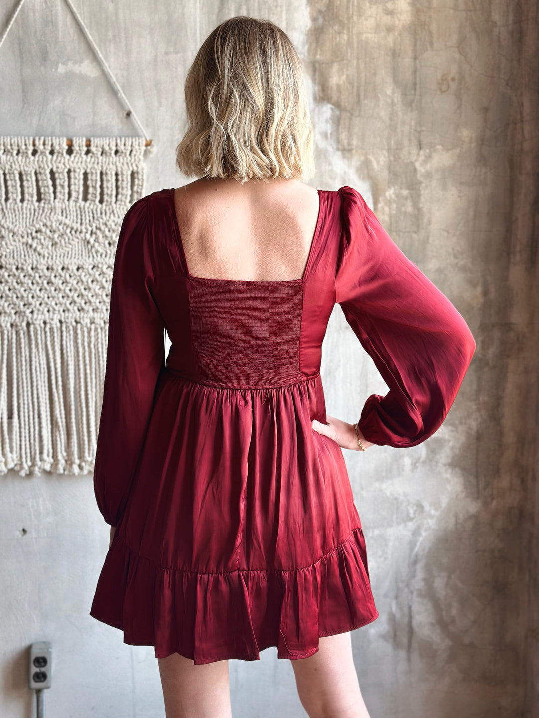 Person wearing a red dress with long sleeves in a neutral setting