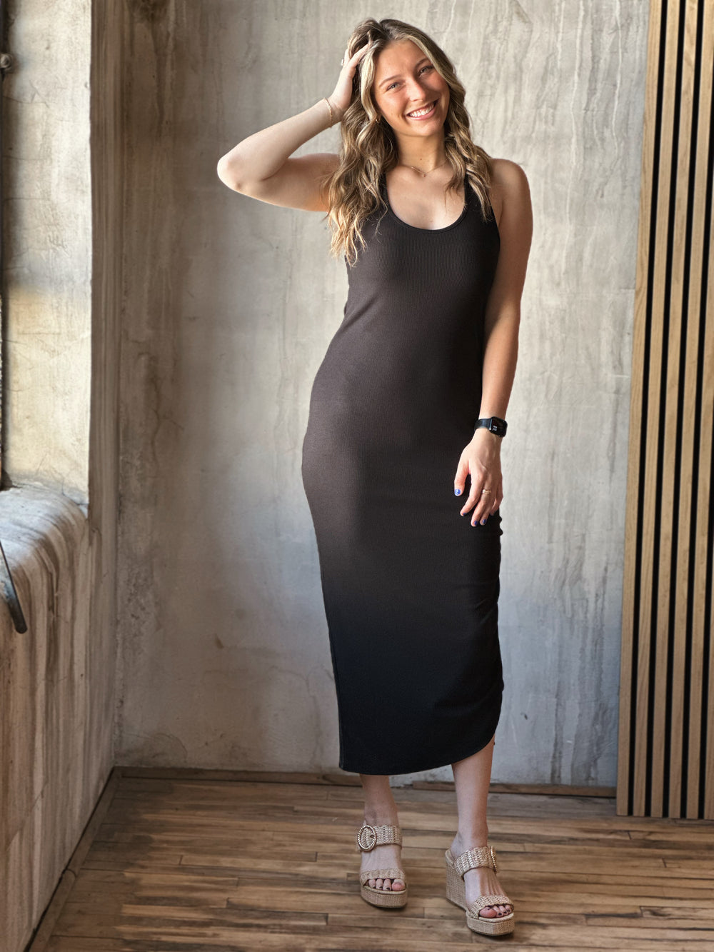 Front view of model wearing a black midi dress with a scoop neckline, sleeveless design and adjustable drawstrings along with a knotted open back detail