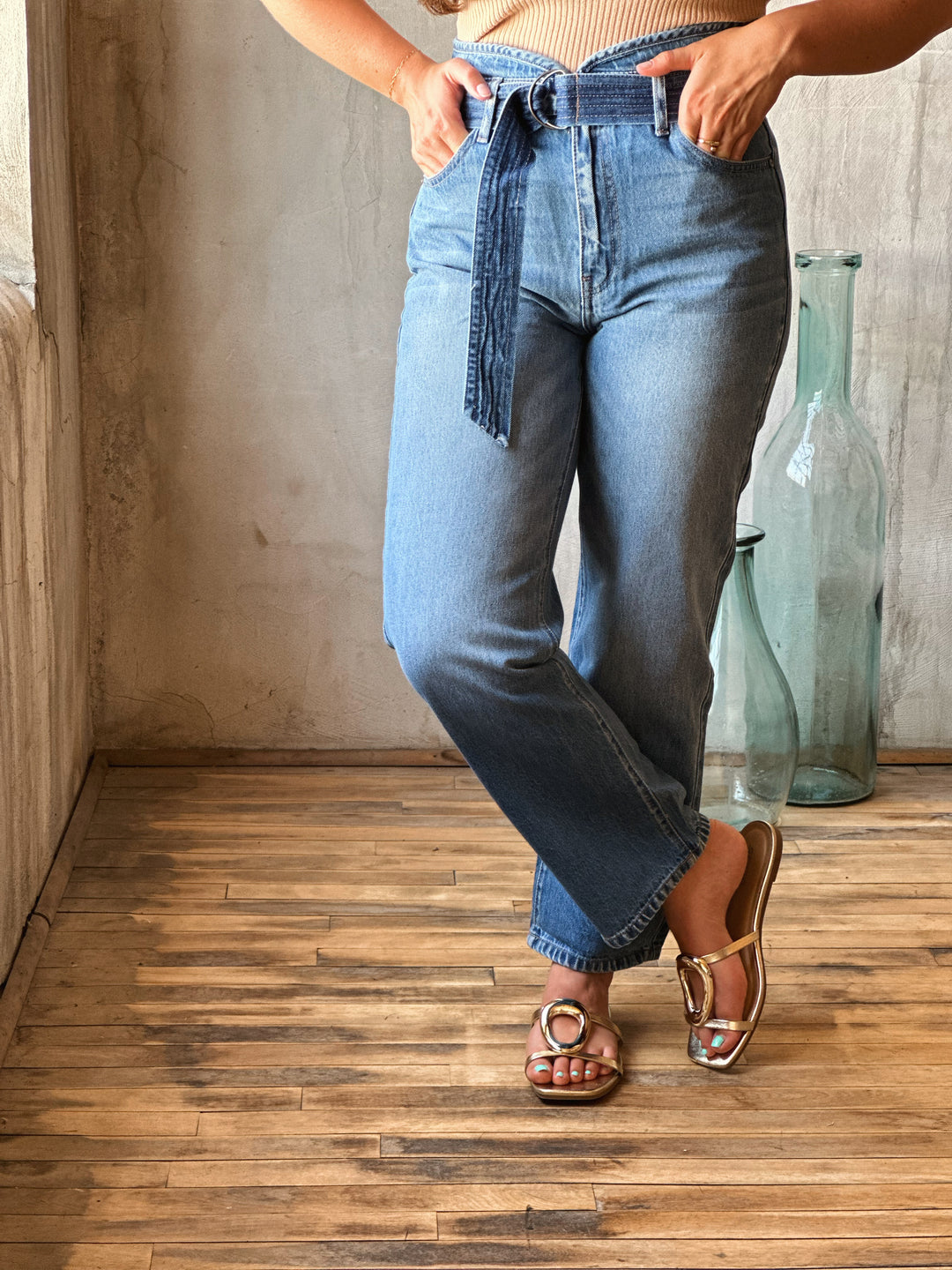 Person wearing blue jeans standing on a wooden floor with a neutral wall background