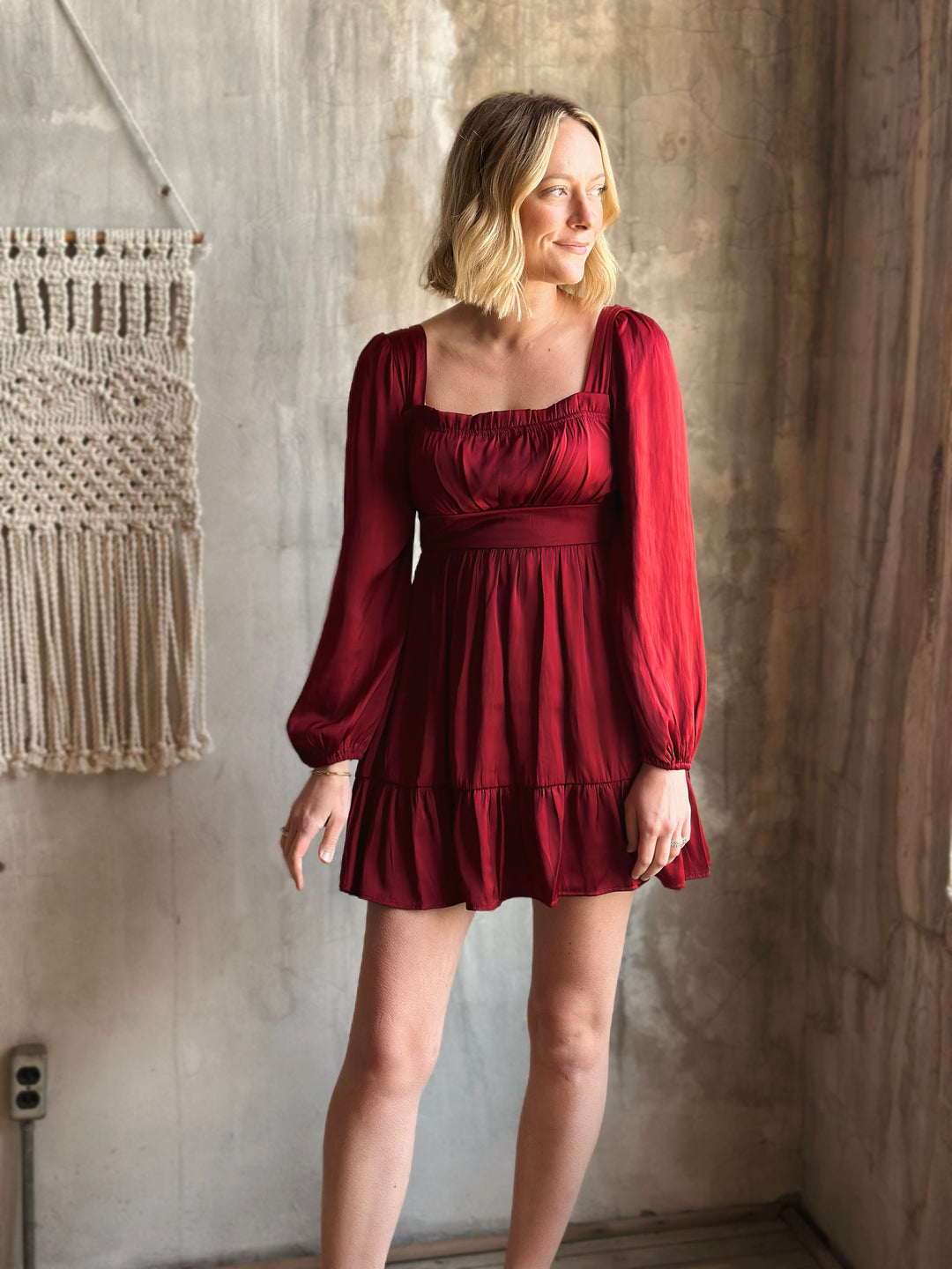 Woman wearing a red dress standing against a textured wall.