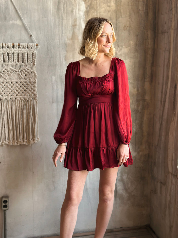 Woman wearing a red dress standing against a textured wall.
